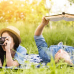 young-cheerful-woman-taking-photo-man-reading-book-grass